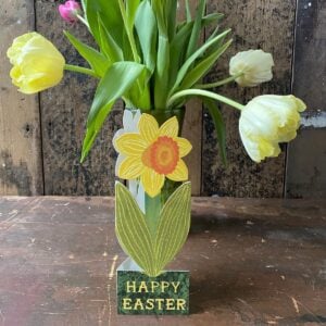 Daffodil shaped Easter greetings card in front of a vase of yellow tulips