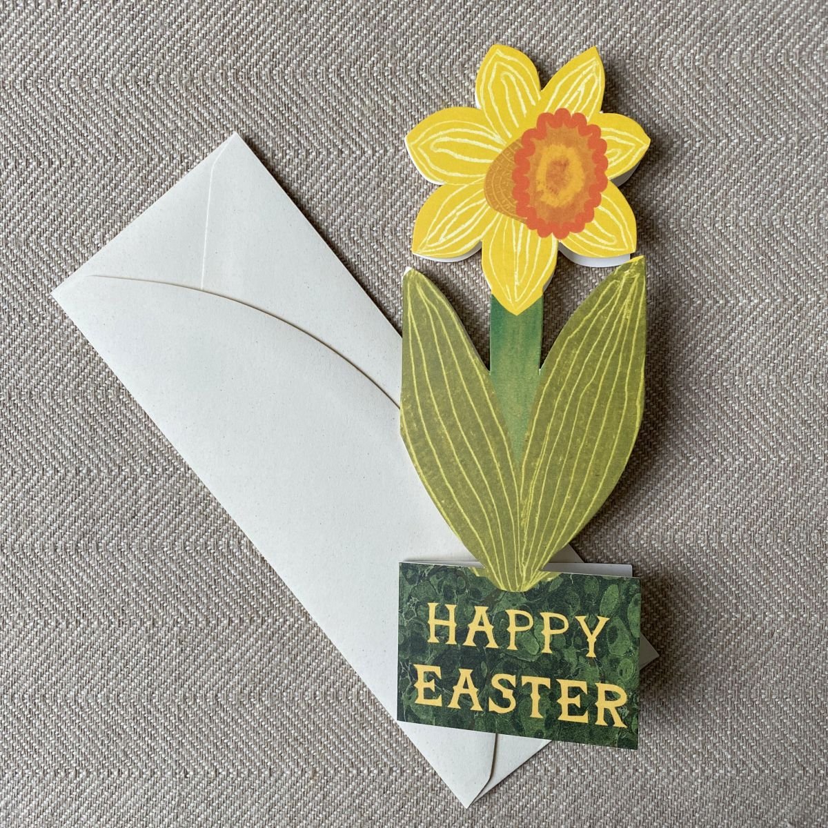 Daffodil shaped greetings card & cream envelope on neutral background