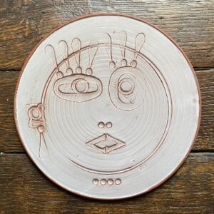 Round, decorative plate with face made from letterpress block impressions on a wooden floor