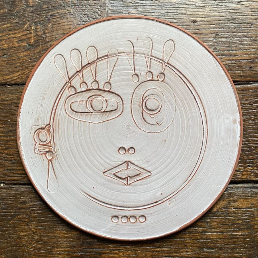 Round, decorative plate with face made from letterpress block impressions on a wooden floor