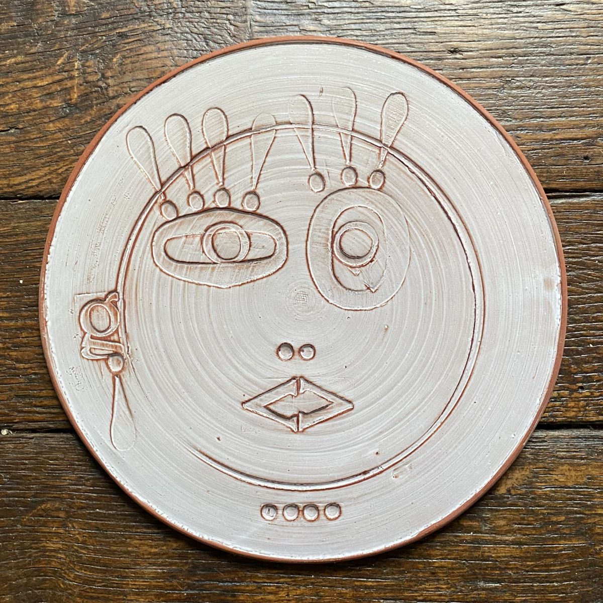 Round, decorative plate with face made from letterpress block impressions on a wooden floor