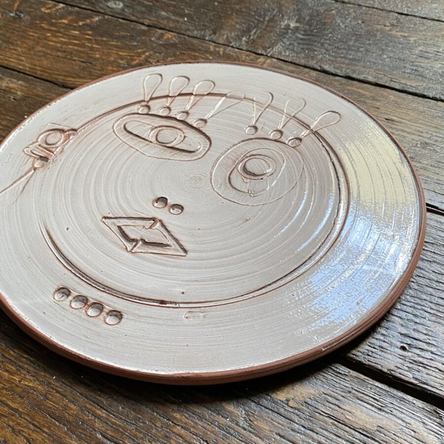 Round, decorative plate with face made from letterpress block impressions on a wooden floor