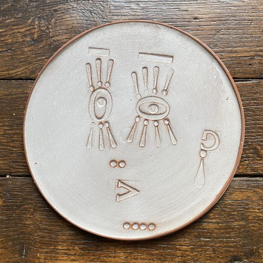 Round, decorative plate with face made from letterpress block impressions on a wooden floor