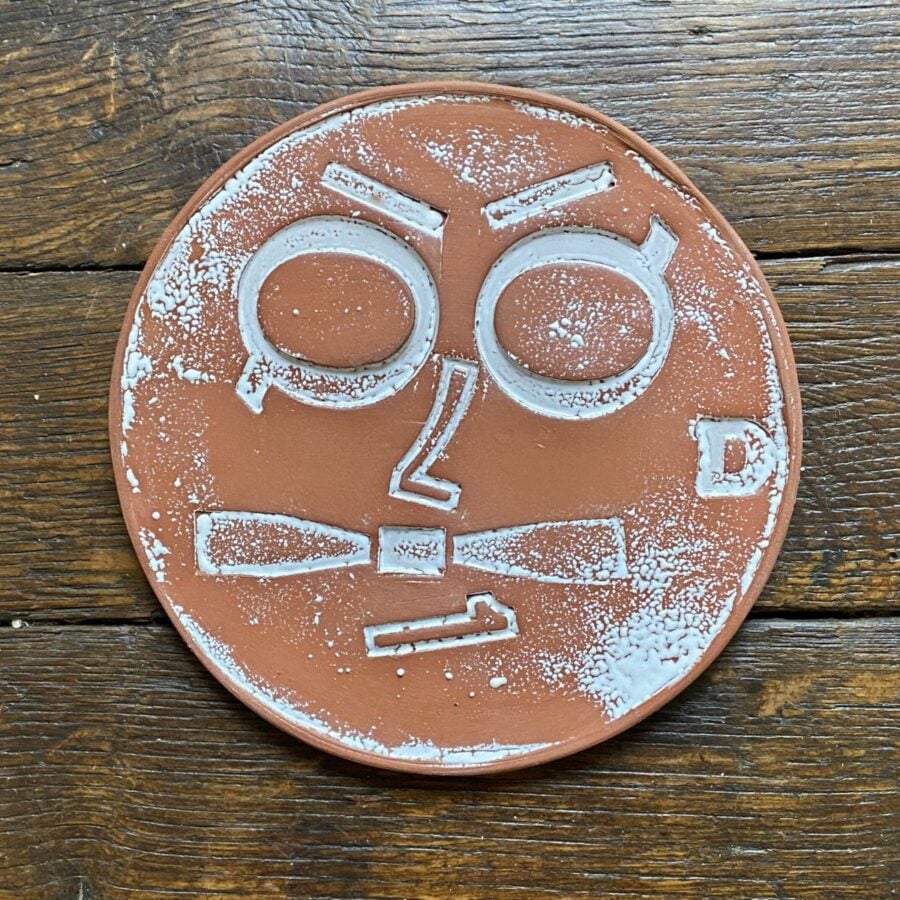 Round, decorative plate with face made from letterpress block impressions on a wooden floor
