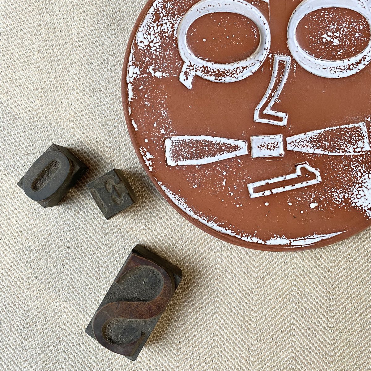 Round, decorative plate with face made from letterpress block impressions on a neutral fabric base