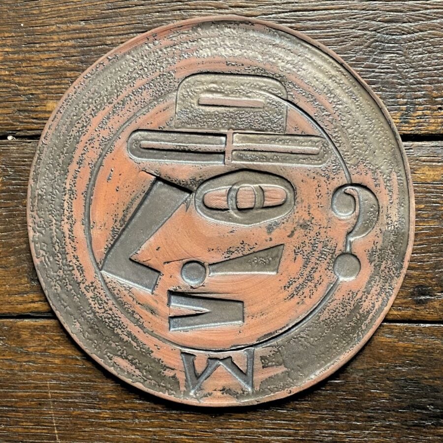 Round, decorative plate with face made from letterpress block impressions on a wooden floor
