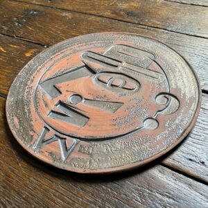 Round, decorative plate with face made from letterpress block impressions on a wooden floor