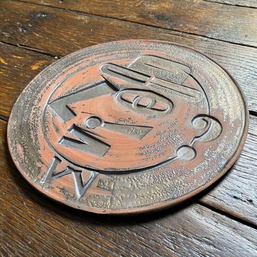 Round, decorative plate with face made from letterpress block impressions on a wooden floor
