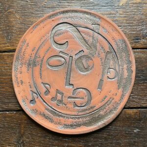 Round, decorative plate with face made from letterpress block impressions on a wooden floor