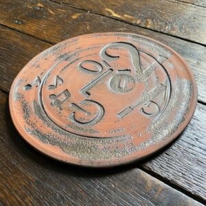 Round, decorative plate with face made from letterpress block impressions on a wooden floor