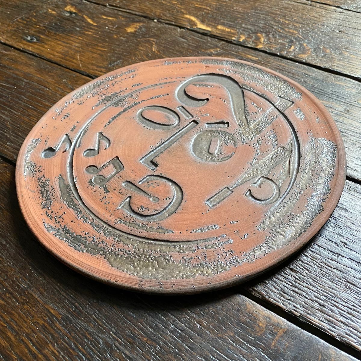 Round, decorative plate with face made from letterpress block impressions on a wooden floor