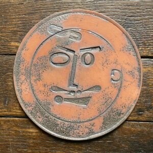 Round, decorative plate with face made from letterpress block impressions on a wooden floor