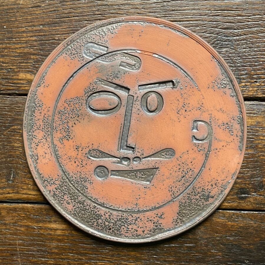 Round, decorative plate with face made from letterpress block impressions on a wooden floor