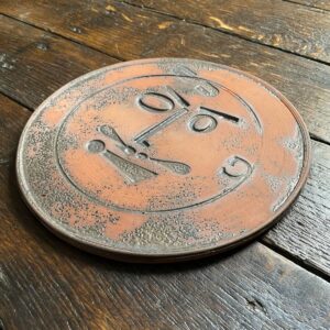 Round, decorative plate with face made from letterpress block impressions on a wooden floor