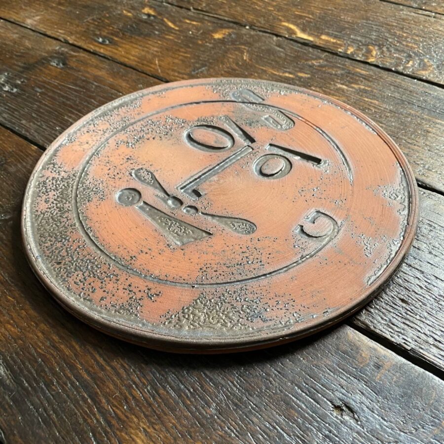 Round, decorative plate with face made from letterpress block impressions on a wooden floor