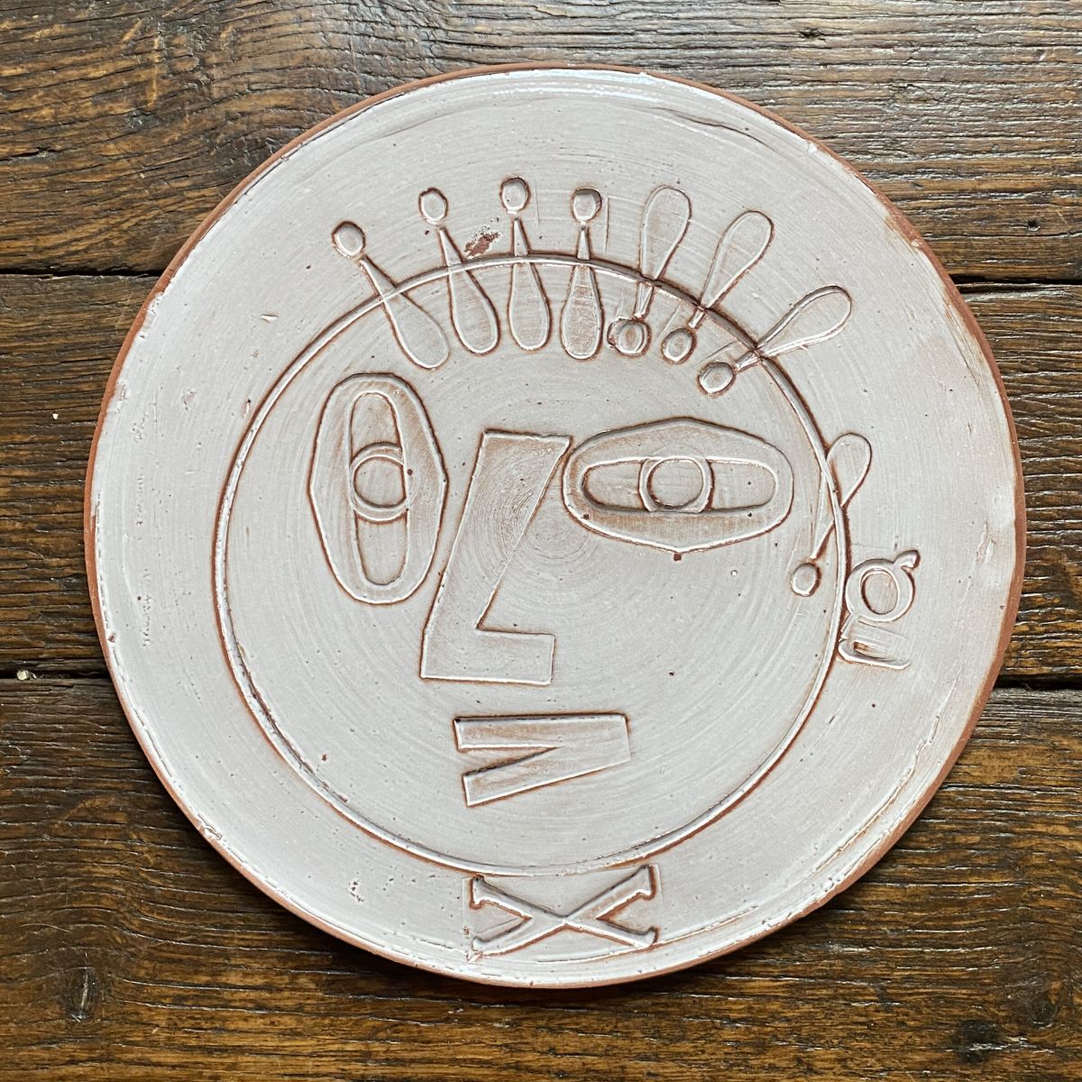 Round, decorative plate with off-white glaze and face made from letterpress block impressions on a wooden floor