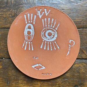 Round, decorative plate with face made from letterpress block impressions on a wooden floor