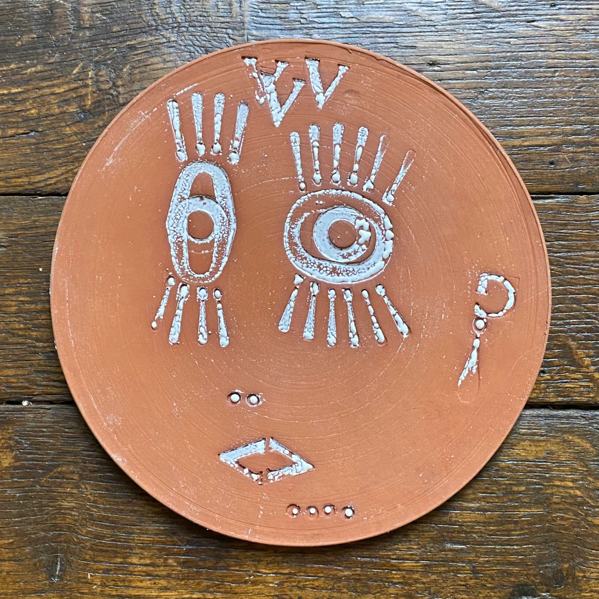 Round, decorative plate with face made from letterpress block impressions on a wooden floor