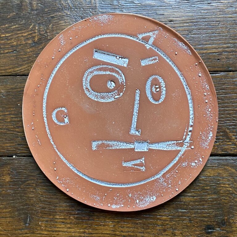 Round, decorative plate with face made from letterpress block impressions on a wooden floor