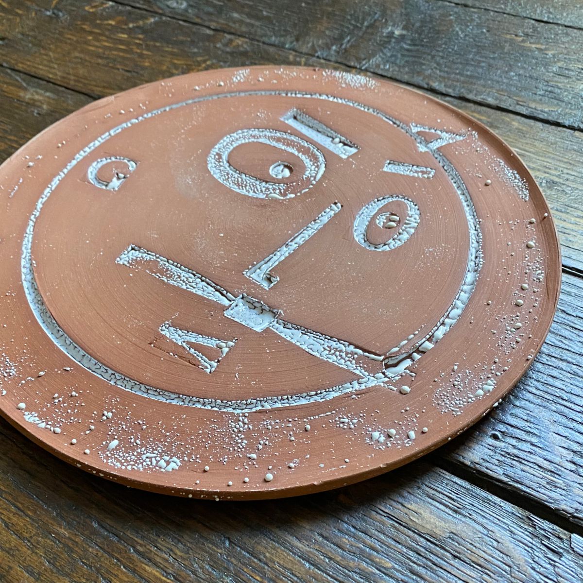 Round, decorative plate with face made from letterpress block impressions on a wooden floor