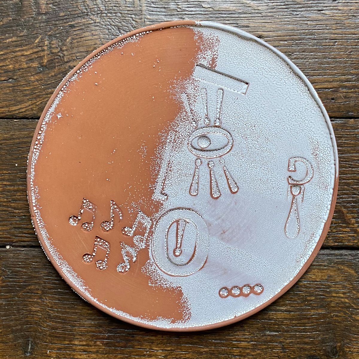 Round, decorative plate with face made from letterpress block impressions on a wooden floor