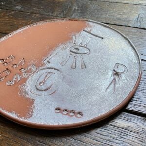 Round, decorative plate with face made from letterpress block impressions on a wooden floor