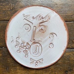 Round, decorative plate with face made from letterpress block impressions on a wooden floor