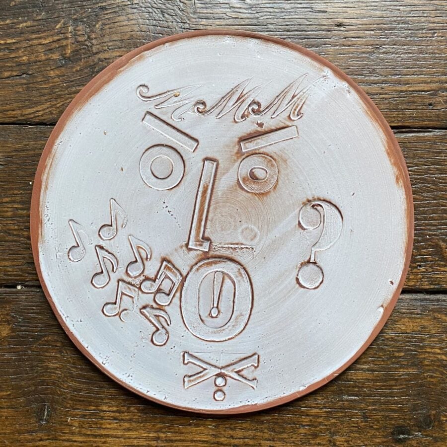 Round, decorative plate with face made from letterpress block impressions on a wooden floor