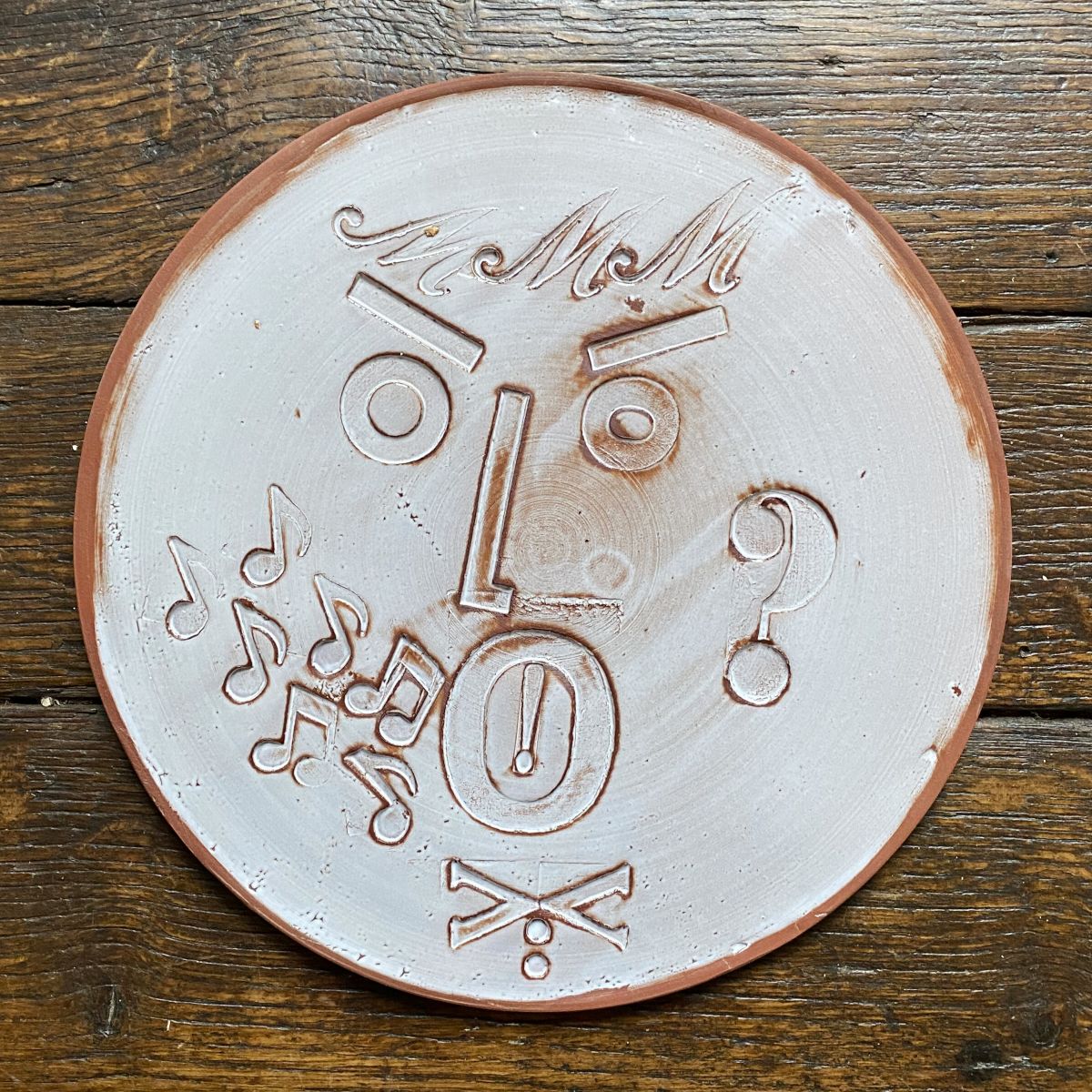Round, decorative plate with face made from letterpress block impressions on a wooden floor