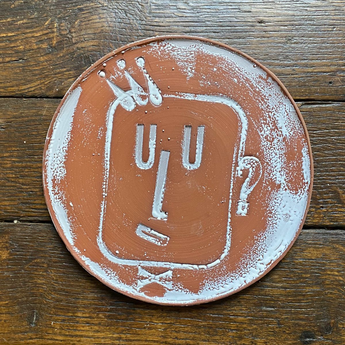 Round, decorative plate with face made from letterpress block impressions on a wooden floor
