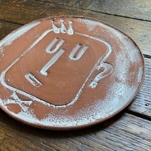 Round, decorative plate with face made from letterpress block impressions on a wooden floor