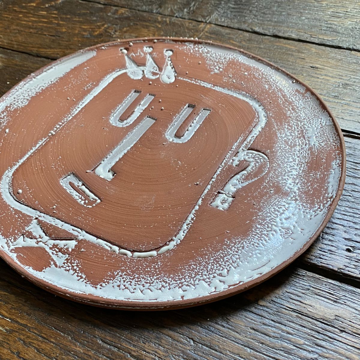 Round, decorative plate with face made from letterpress block impressions on a wooden floor