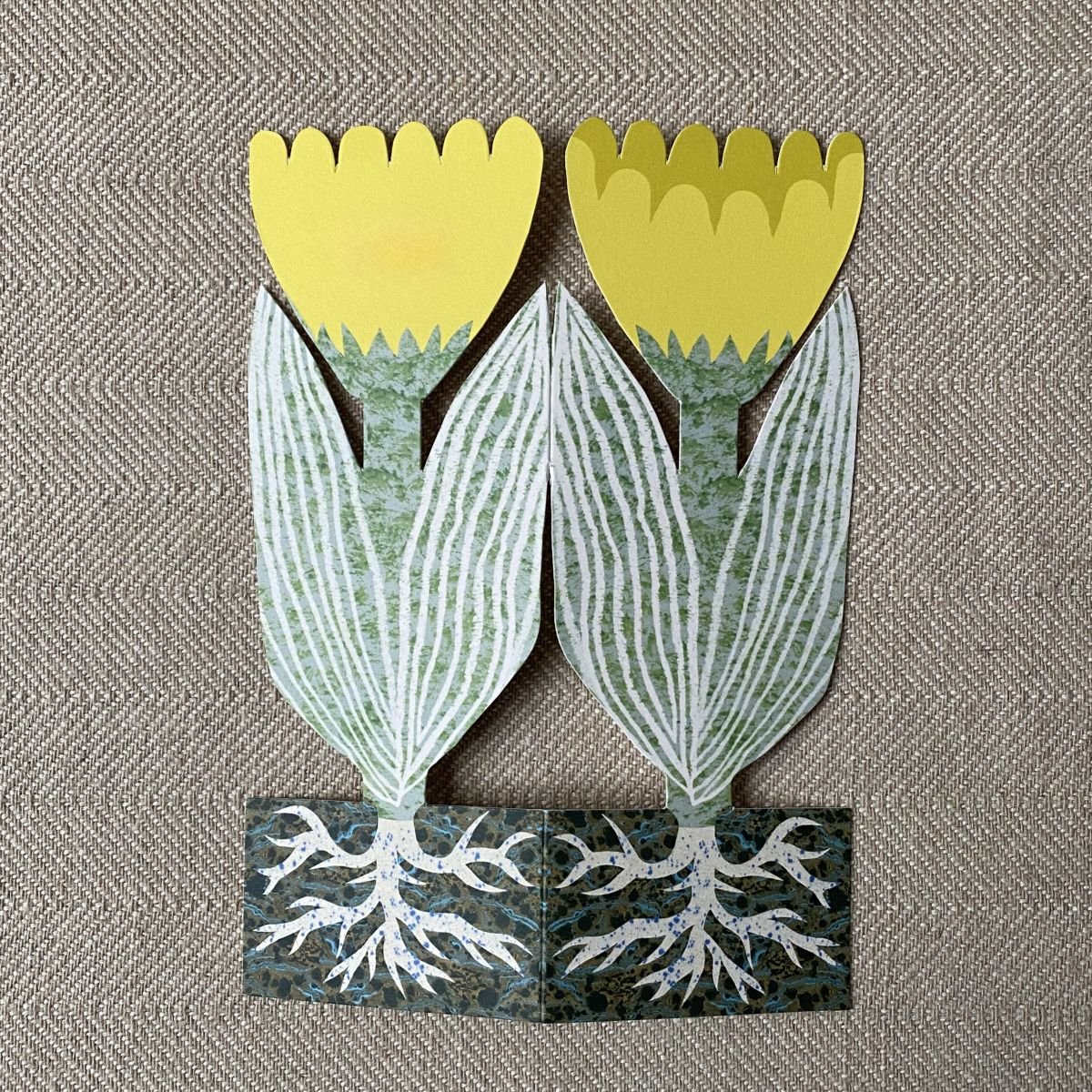 Splayed yellow tulip shaped greetings card on a neutral background