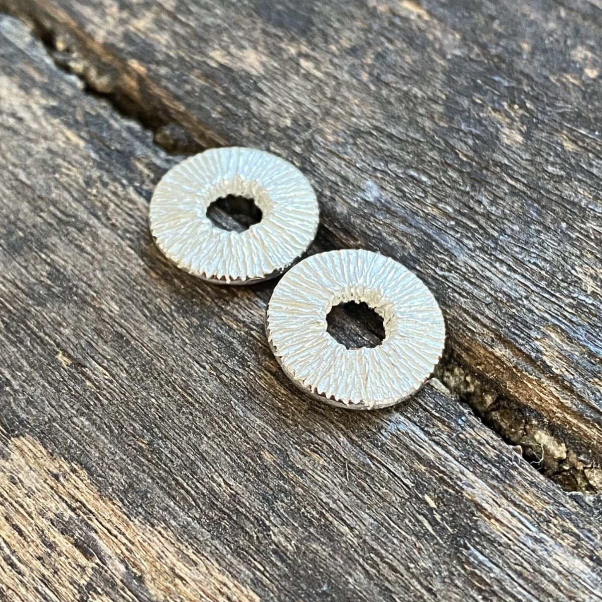 Silver cog earrings on a wooden background