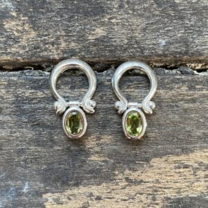 Silver drop earrings with peridot centres on a wooden background