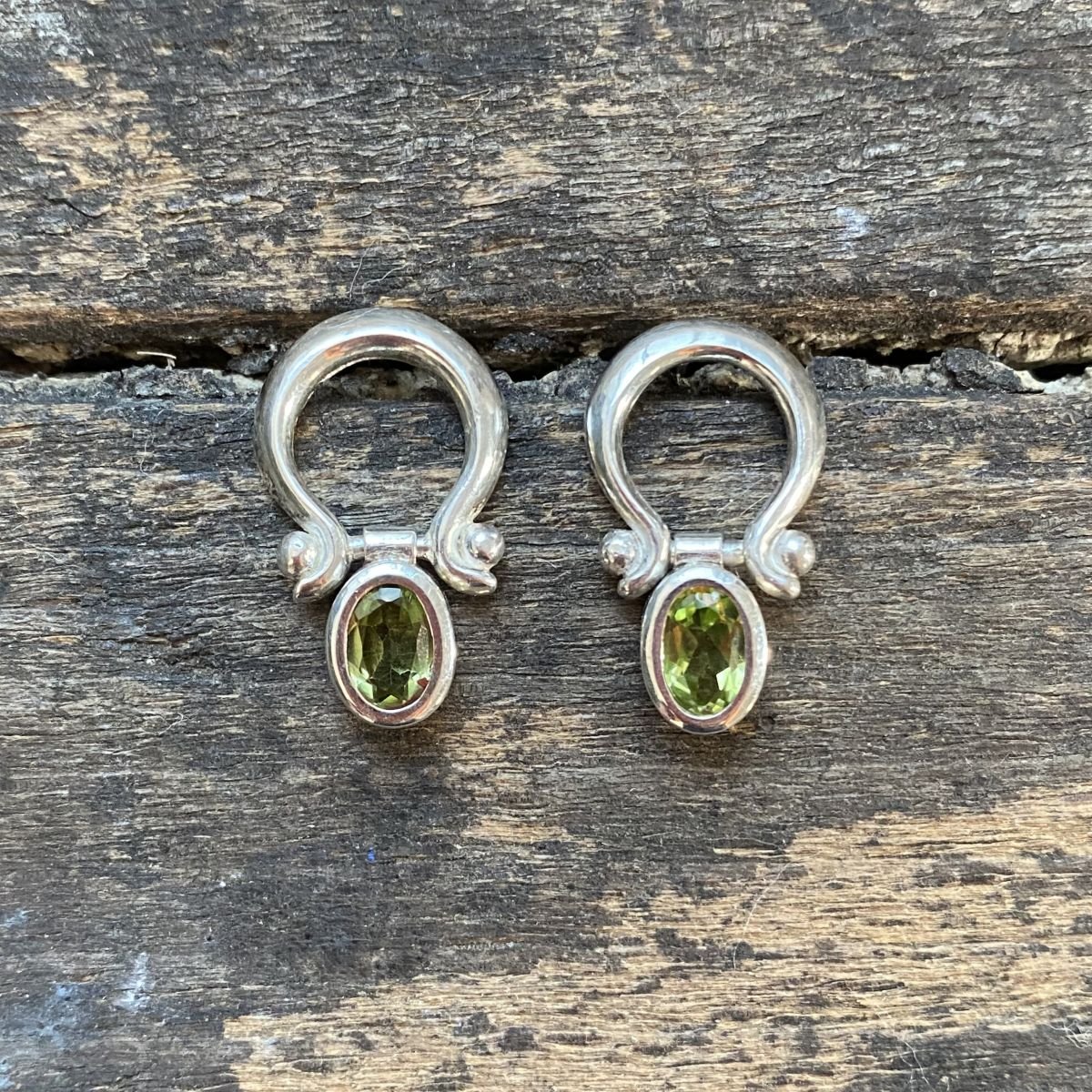 Silver drop earrings with peridot centres on a wooden background