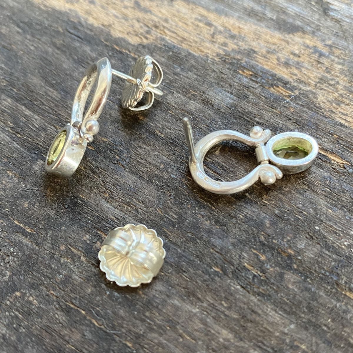 Silver drop earrings with peridot centres on a wooden background
