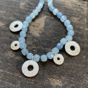 Silver and aquamarine necklace by Clare de la Torre on a wooden background