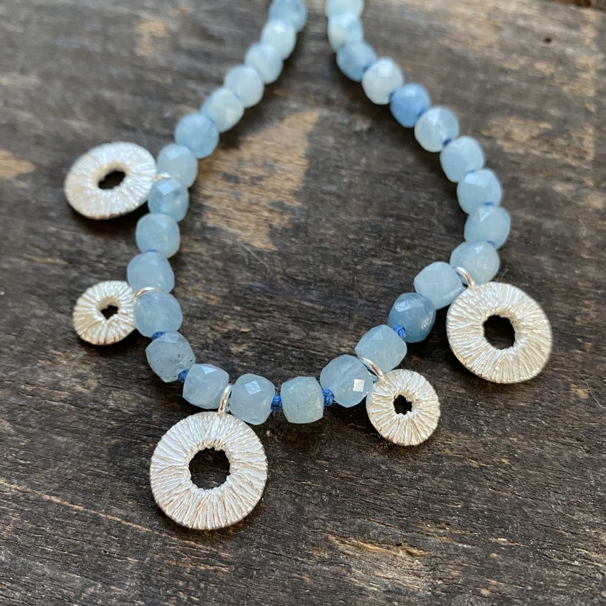 Silver and aquamarine necklace by Clare de la Torre on a wooden background