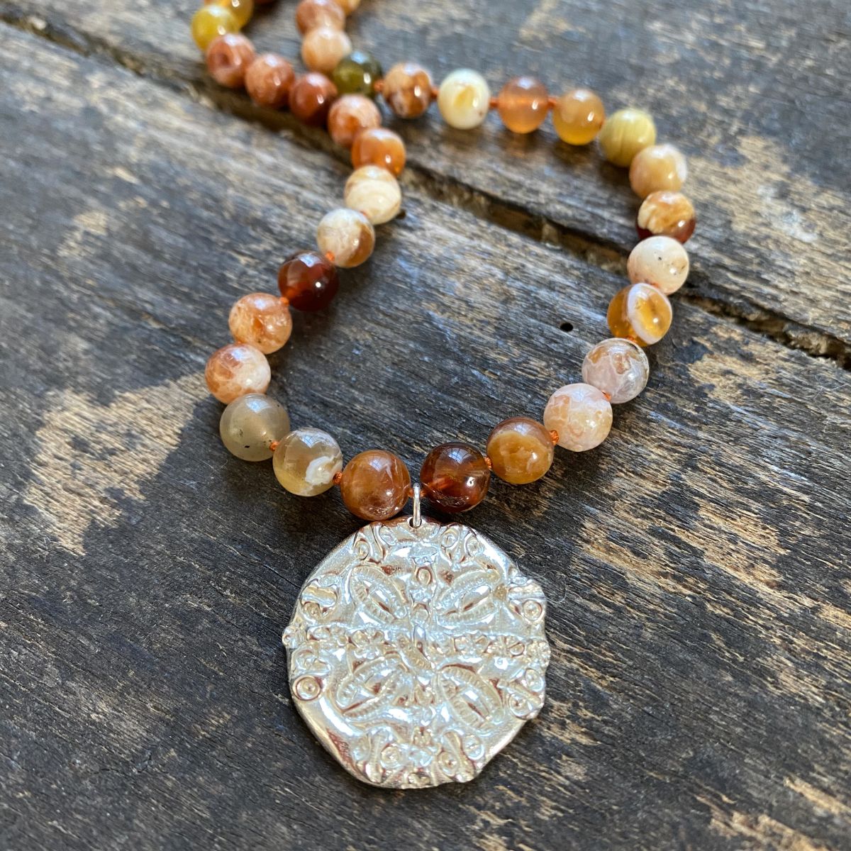 Brandy opal gemstone necklace by Clare de la Torre on a wooden background