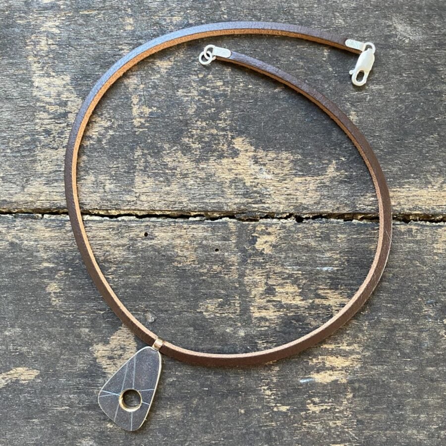 silver pendant on a leather thong necklace by Clare de la Torre on a wooden background