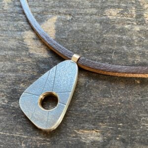 silver pendant on a leather thong necklace by Clare de la Torre on a wooden background
