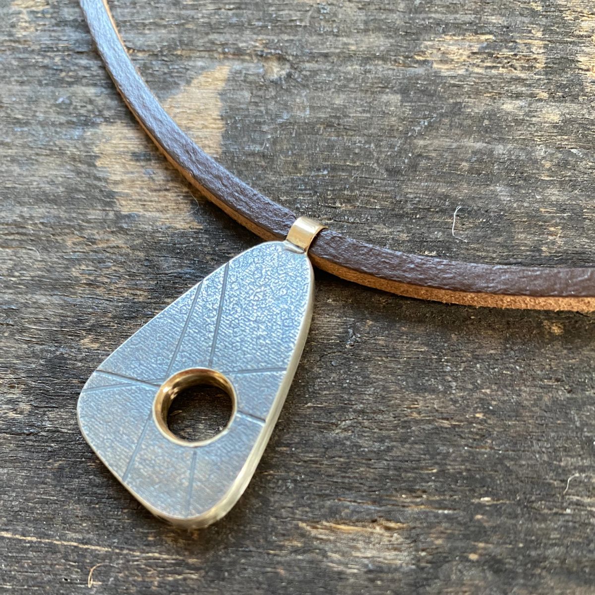 silver pendant on a leather thong necklace by Clare de la Torre on a wooden background