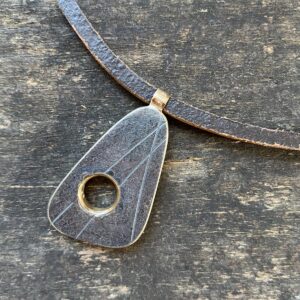 silver pendant on a leather thong necklace by Clare de la Torre on a wooden background