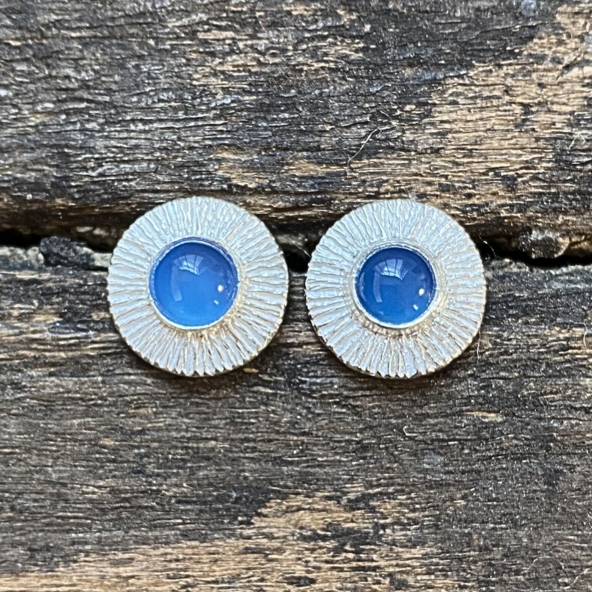 Silver cog earrings with blue stone on a wooden background