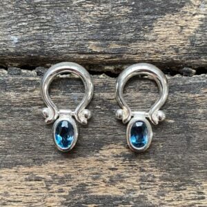 Silver drop earrings with blue topaz gemstones on wooden background