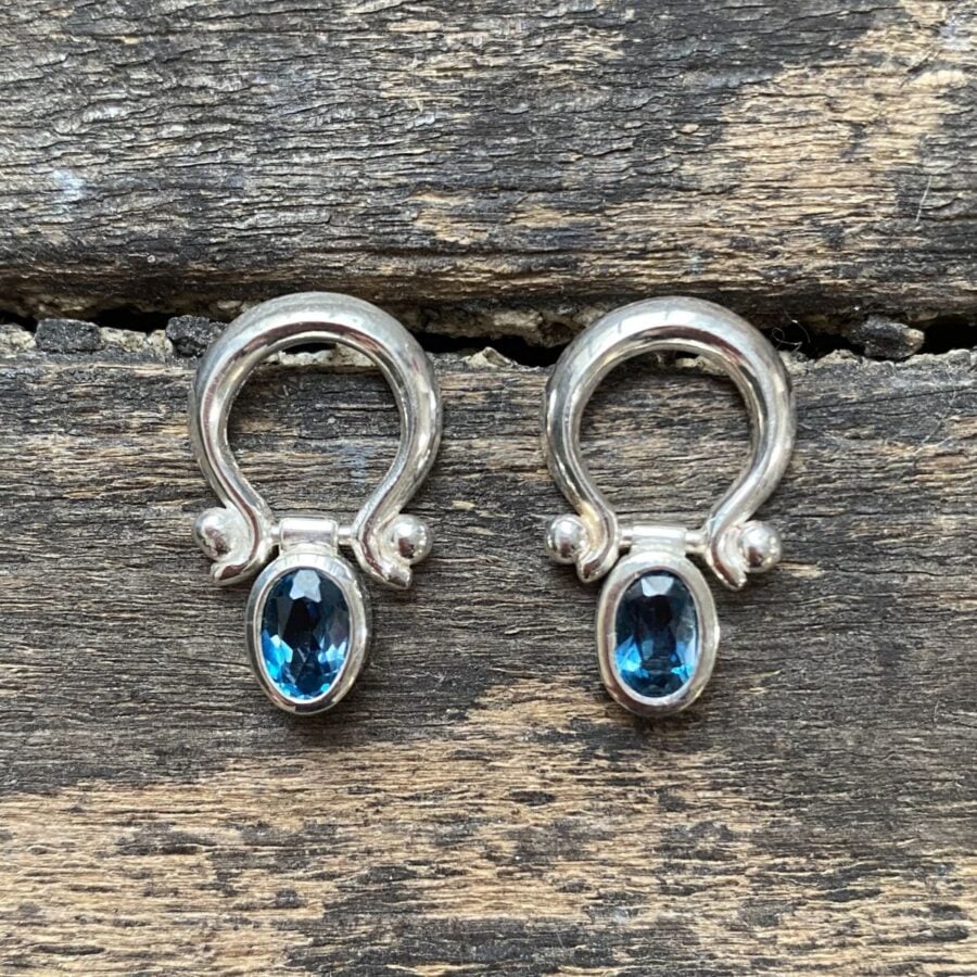 Silver drop earrings with blue topaz gemstones on wooden background