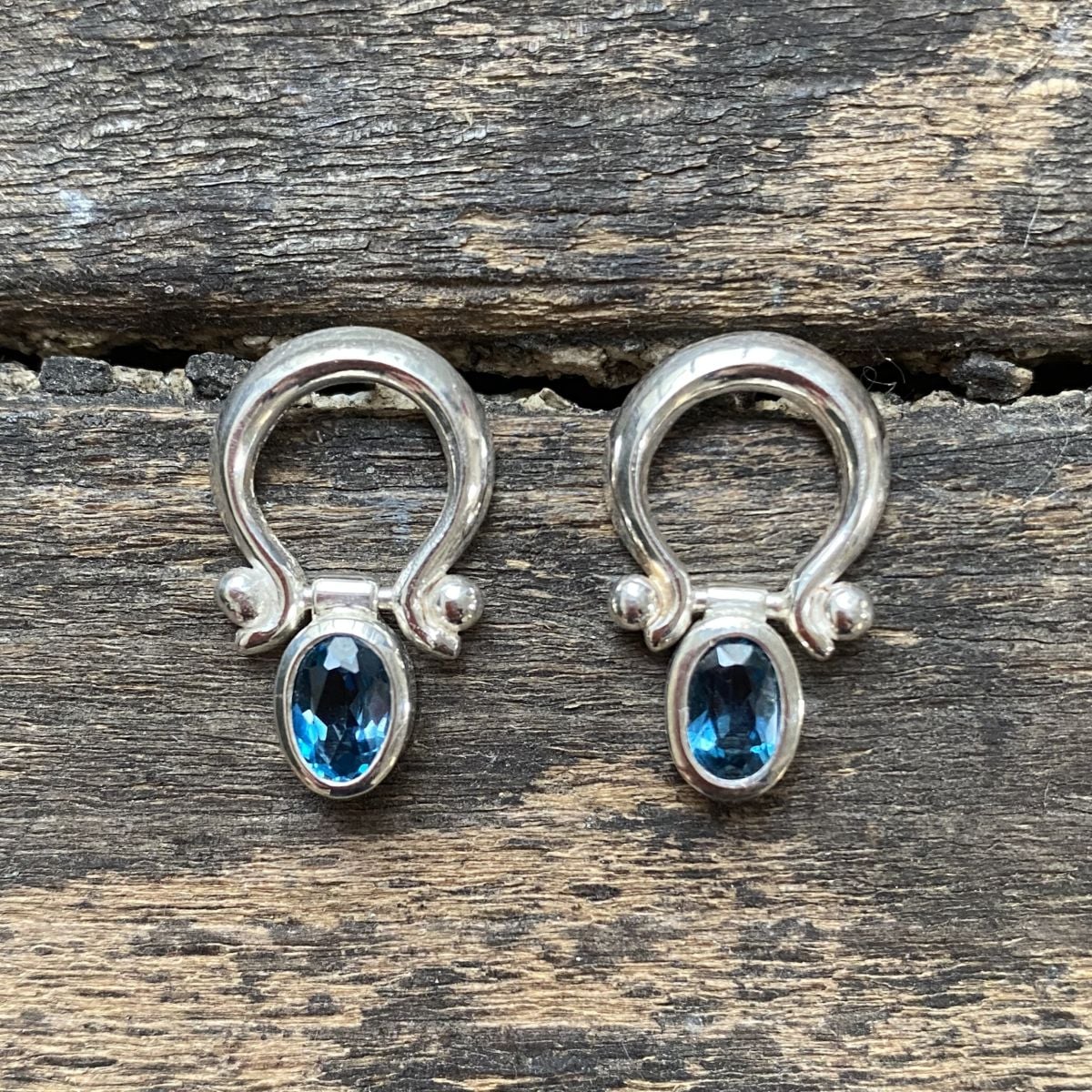 Silver drop earrings with blue topaz gemstones on wooden background