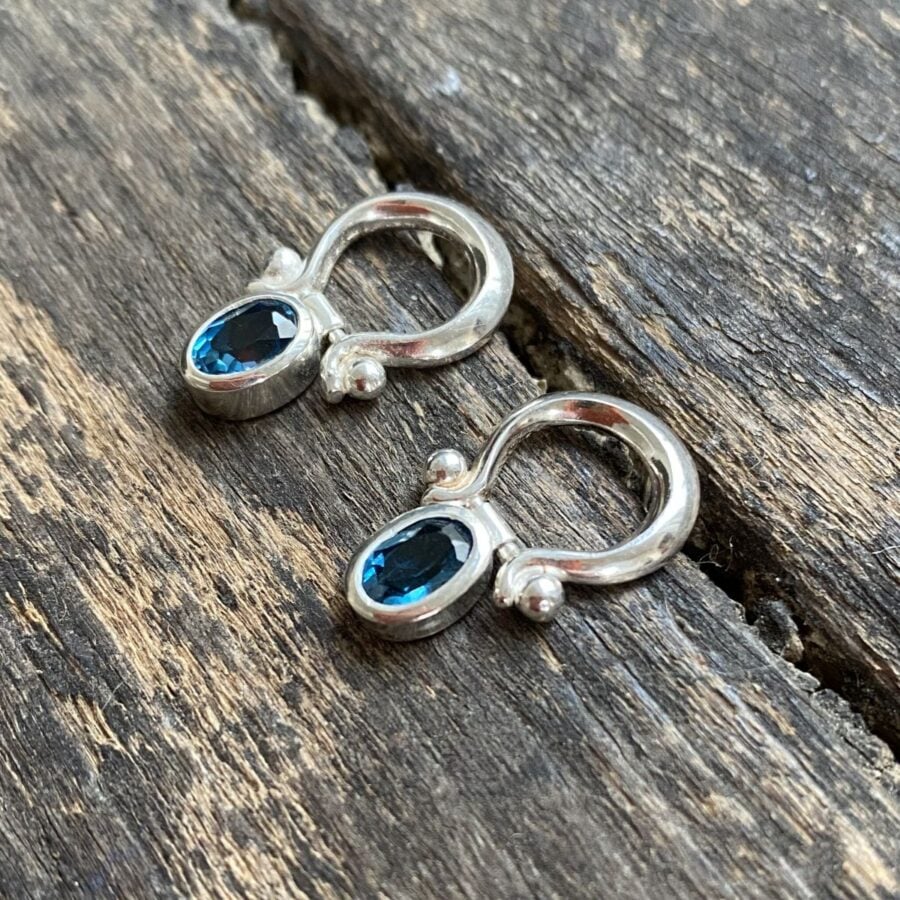 Silver drop earrings with blue topaz gemstones on wooden background