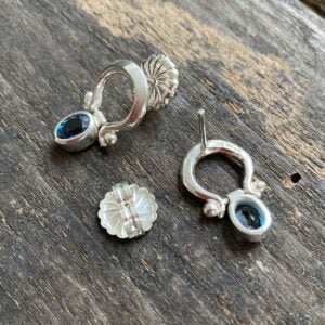 Silver drop earrings with blue topaz gemstones on wooden background